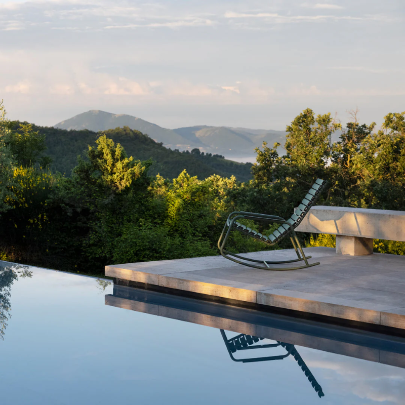 The ReClips Outdoor Rocking Chair from Houe by a pool with a scenic mountain view.