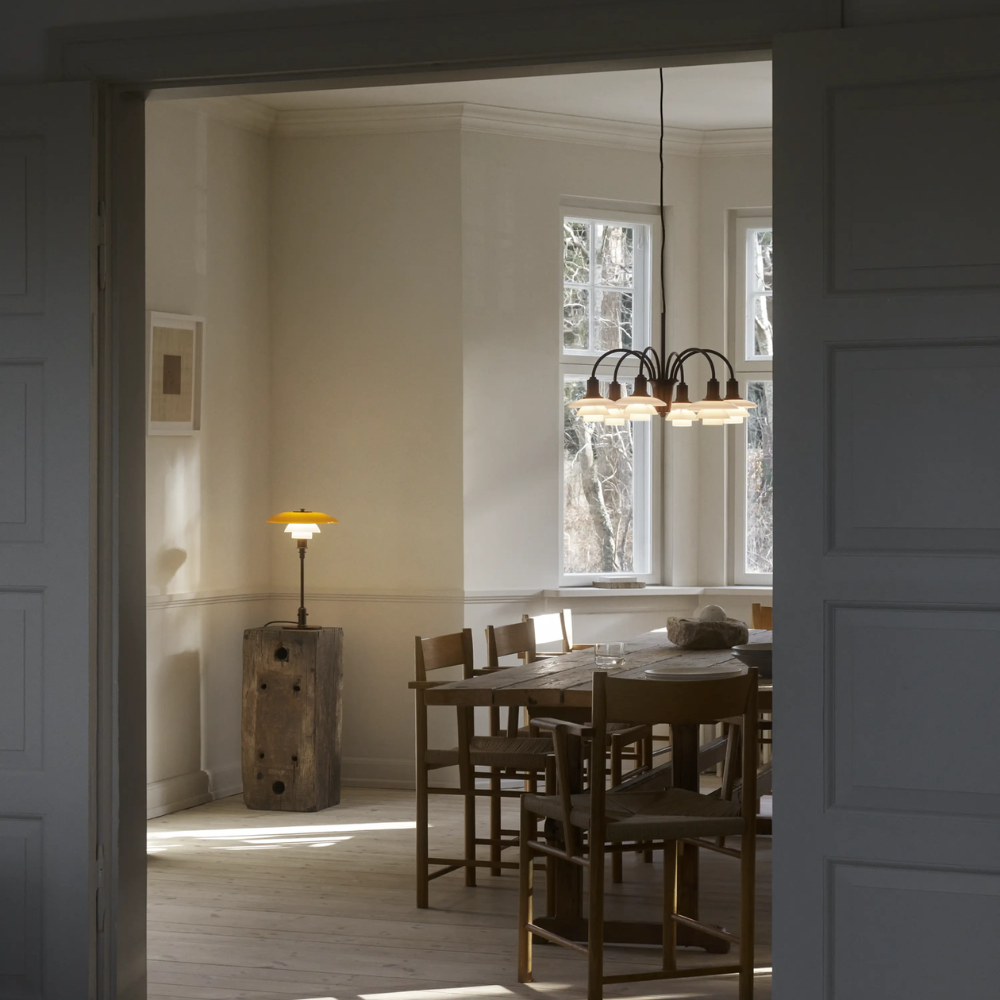 The PH 1/1 Chandelier, 6-Light by Louis Poulsen in a dining room turned on.