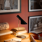 The AJ Mini Table Lamp in Brass/Black on a desk.