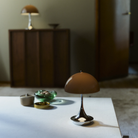 The Panthella 160 Portable Lamp from Louis Poulsen in Original Opal Brown on a table turned on.