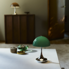 The Panthella 160 Portable Lamp from Louis Poulsen in Original Opal Green on a table turned on.