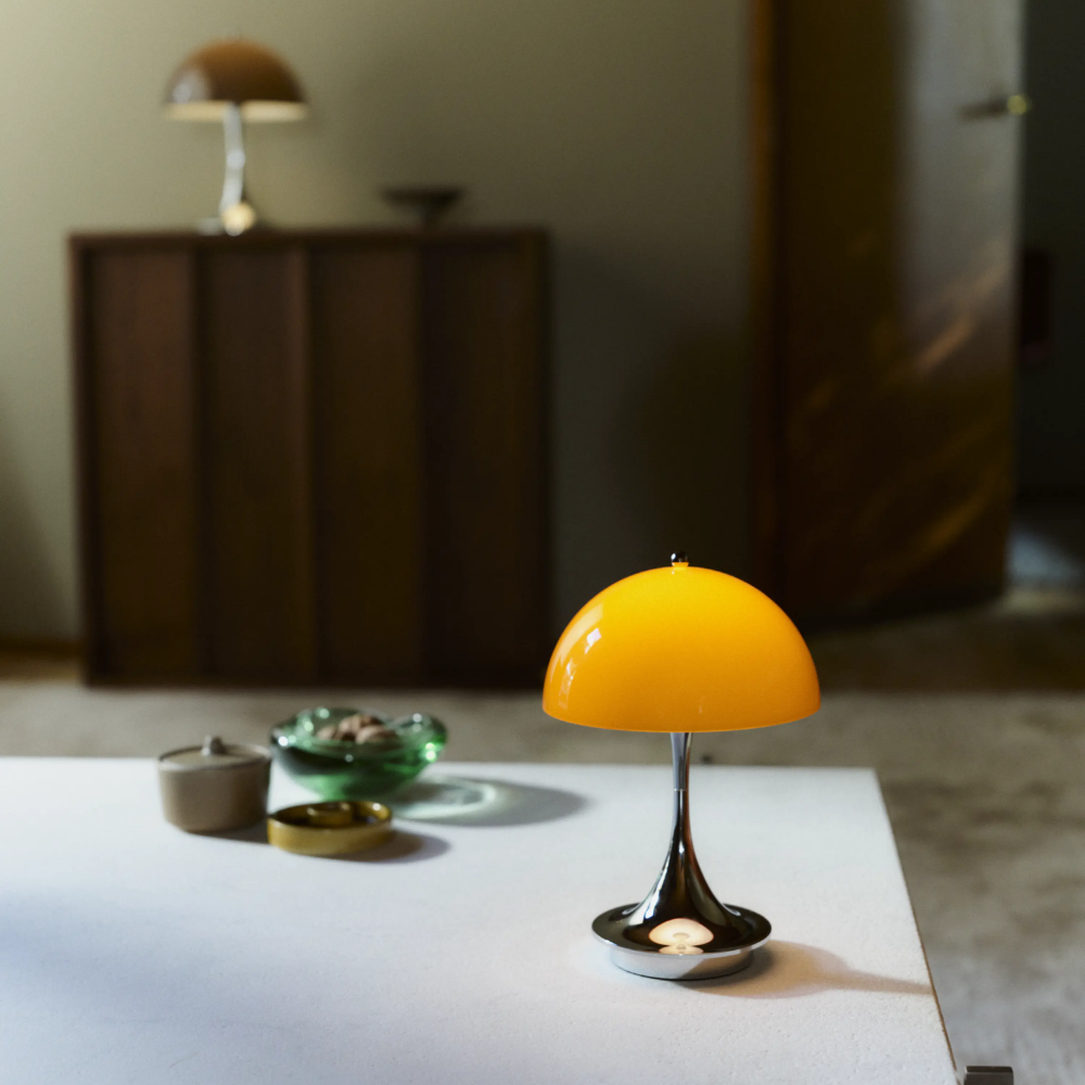 The Panthella 160 Portable Lamp from Louis Poulsen in Original Opal Orange on a dining table turned on.