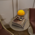 The Panthella 160 Portable Lamp from Louis Poulsen in Original Opal Orange on a side table turned on.