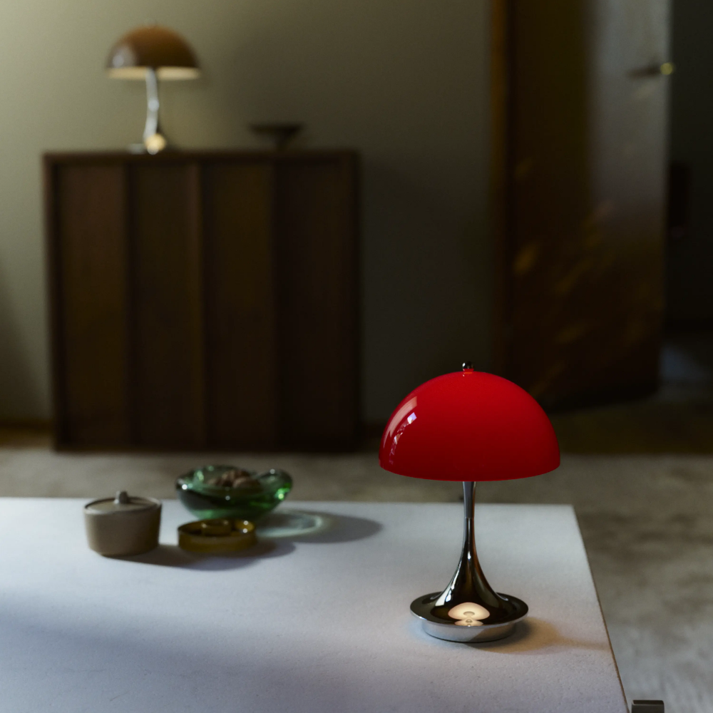 The Panthella 160 Portable Lamp from Louis Poulsen in Original Opal Red on a table turned on.