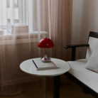 The Panthella 160 Portable Lamp from Louis Poulsen in Original Opal Red on a side table turned off.