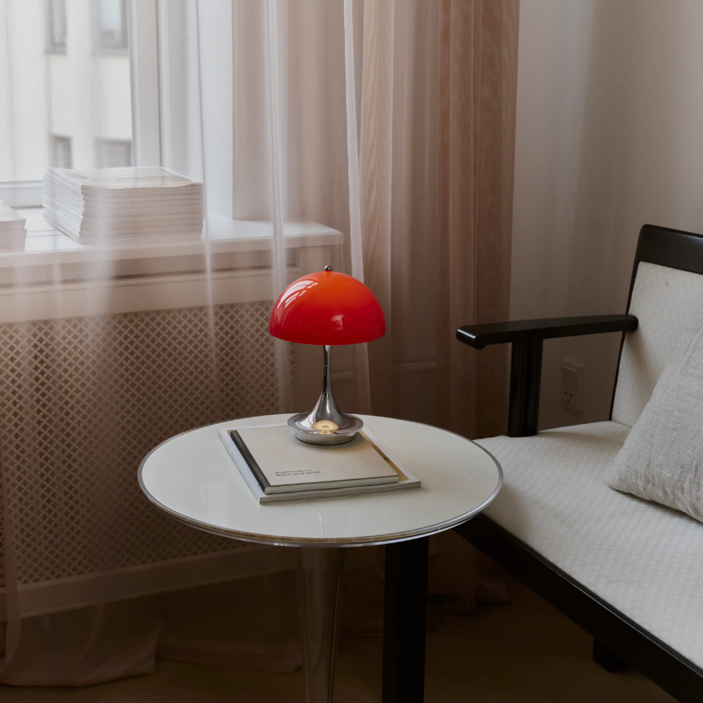 The Panthella 160 Portable Lamp from Louis Poulsen in Original Opal Red on a side table turned on.