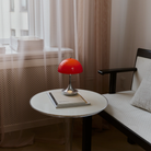 The Panthella 160 Portable Lamp from Louis Poulsen in Original Opal Red on a side table turned on.