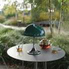 The Panthella 250 Portable Table Lamp from Louis Poulsen in Original Opal Green on an outdoor table turned off.