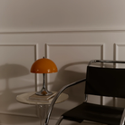The Panthella 250 Portable Table Lamp from Louis Poulsen in Original Opal Orange turned off on a side table.