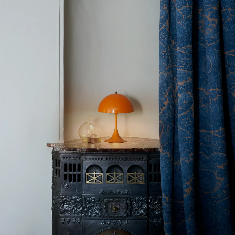 The Panthella 250 Portable Table Lamp from Louis Poulsen in Orange on a side table.