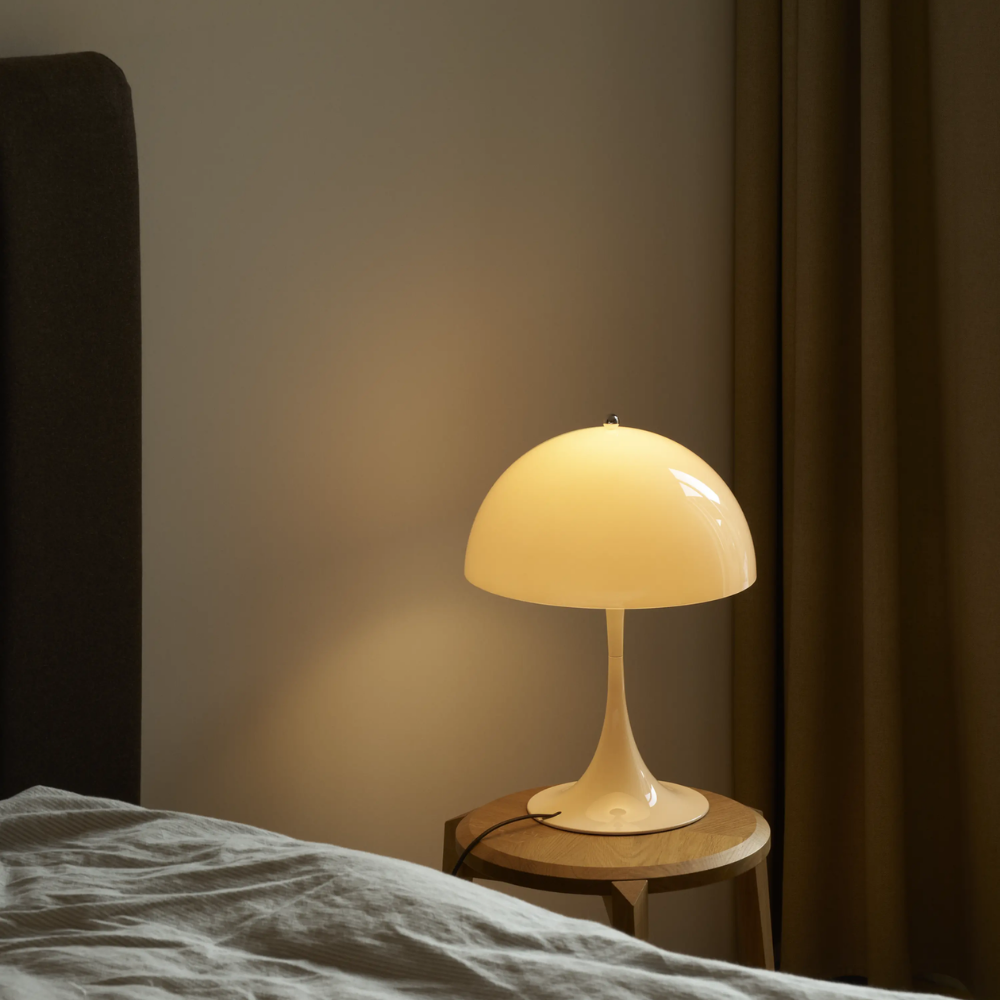 The Panthella 320 Table Lamp from Louis Poulsen in Opal Beige next to a bed turned on