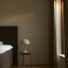 The Panthella 320 Table Lamp from Louis Poulsen in Opal Beige next to a bed.