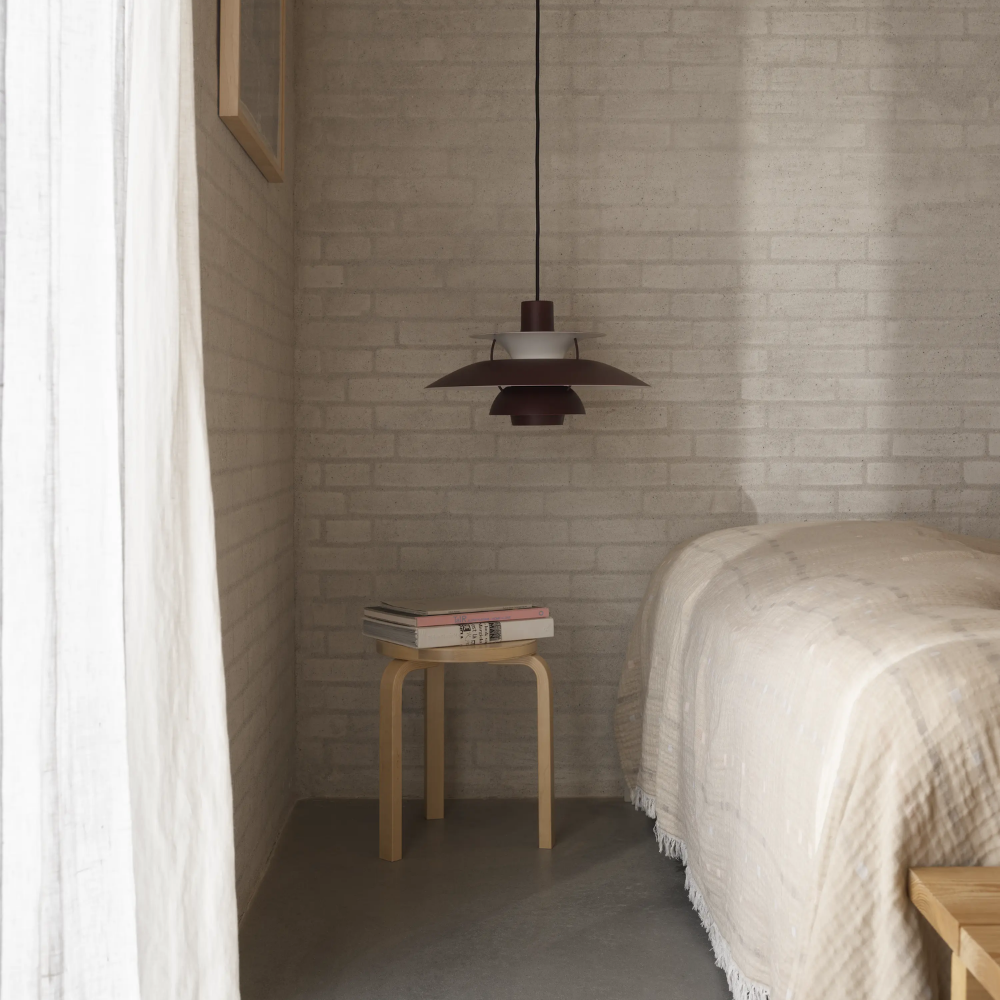 The PH 5 from Louis Poulsen in monochrome burgundy next to a bed.