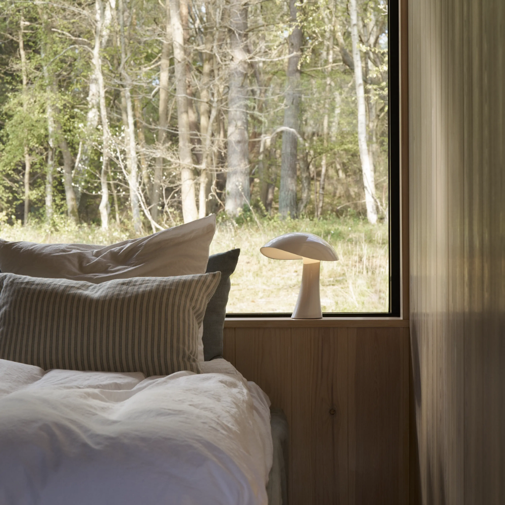 Rumee 220 Portable Lamp in Cloud White next to a bed.