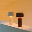 The red wine and off white Bicoca Portable Table Lamp from Marset in a bedroom.
