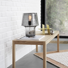 Table lamp on a wooden table with a white brick wall and window in the background