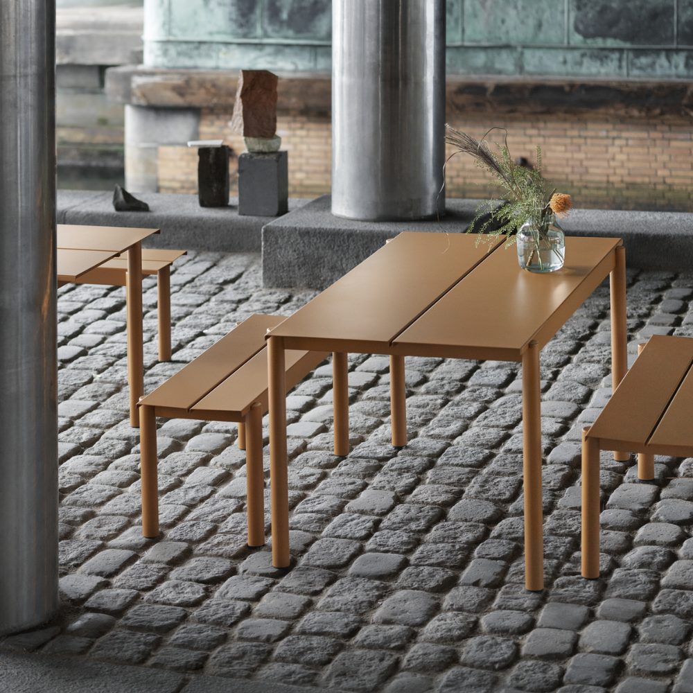 The burnt orange Linear Steel Bench from Muuto in an outdoor dining space.