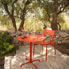 The Pico Round Cafe Table 4-Star Base by Houe is in an outdoor area with a chair on a stone patio with trees and rocks. all-groups