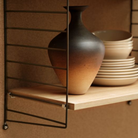 The String System by String Furniture dark brown panels with oak shelves with plates on it.