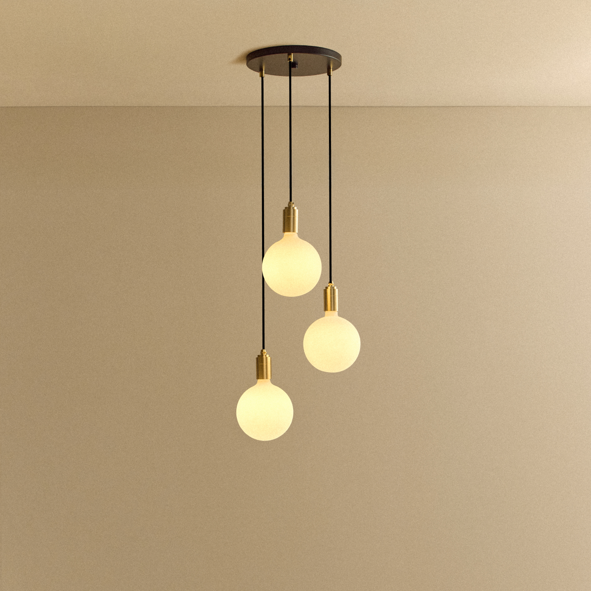 The Triple Pendant in Brass + Sphere IV with black canopy by Tala US in a room.