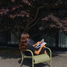 Woman sitting in the Groove Outdoor Lounge Chair by Tom Dixon in Moss.