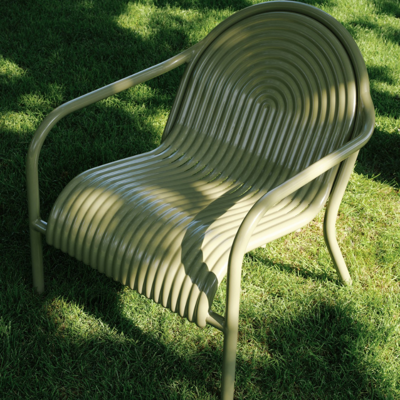 The Groove Outdoor Lounge Chair by Tom Dixon in Moss in a garden.