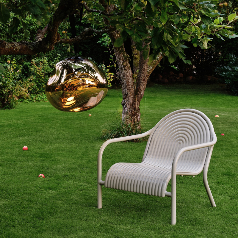 The Groove Outdoor Lounge Chair by Tom Dixon in Putty in a garden with Melt Portable in Bronze.