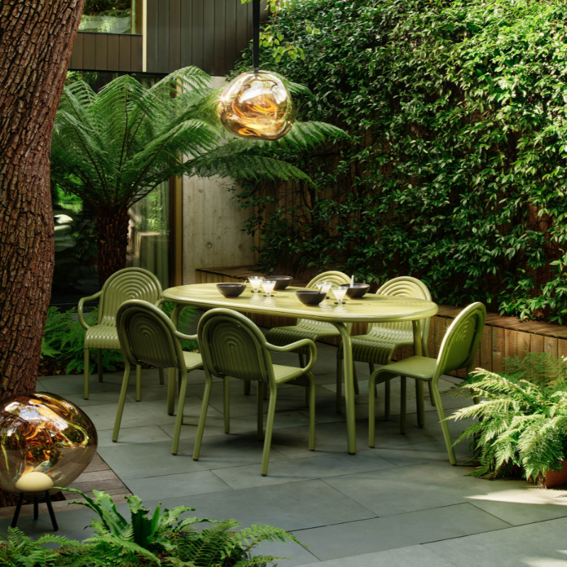 Groove Large Oval Outdoor Table and Chairs in Moss by Tom Dixon in a garden.