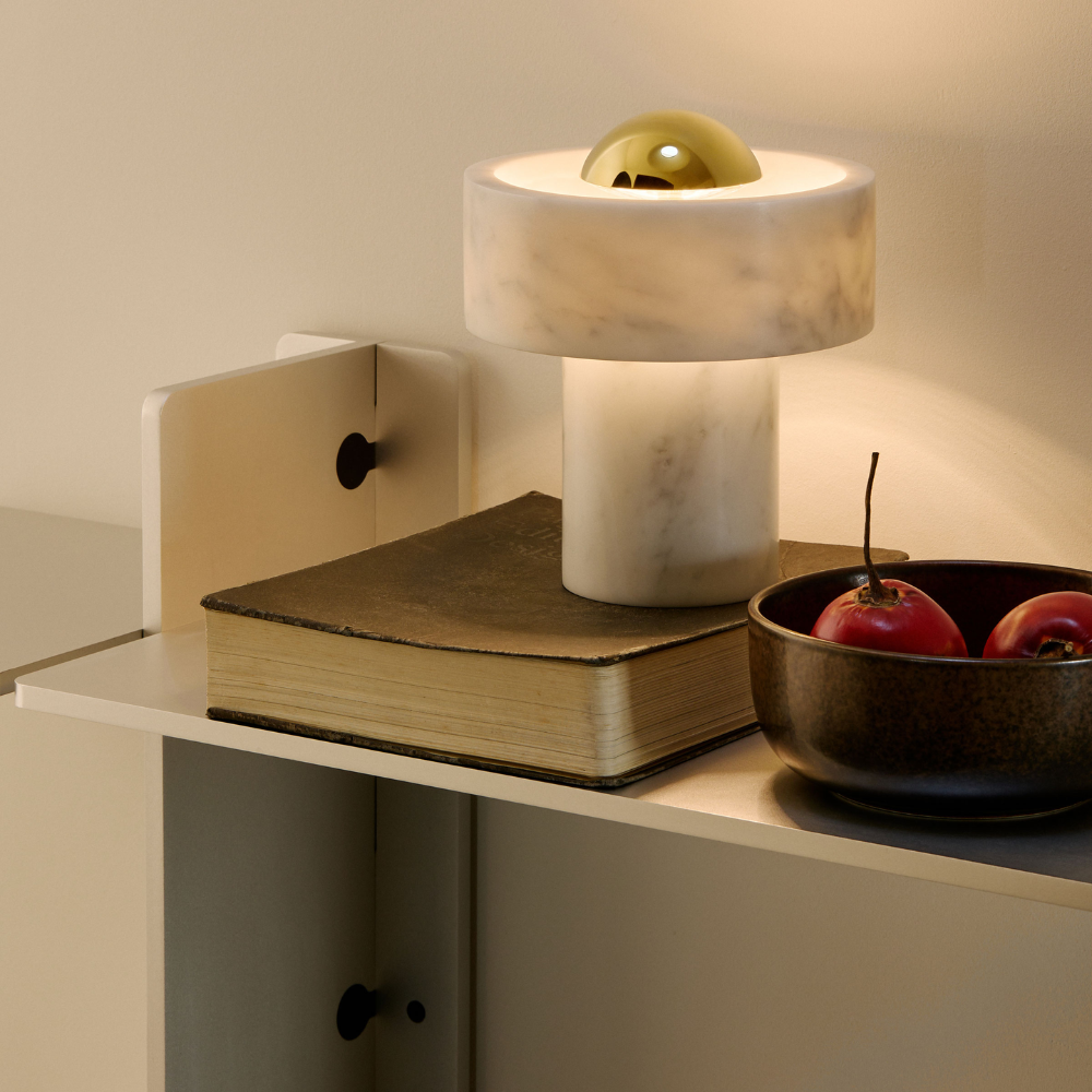 The Stone Portable Light by Tom Dixon in Brass on a shelf.