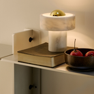 The Stone Portable Light by Tom Dixon in Brass on a shelf.
