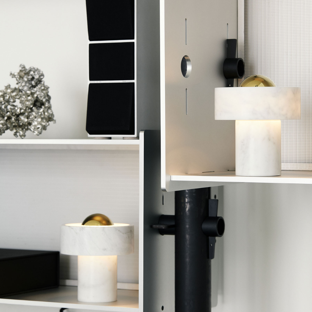 The Stone Portable Light by Tom Dixon in Brass on a bookshelf.
