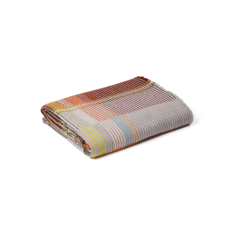 The Joan Throw pairs grey, sienna, and mossy green with yellow and blush highlights in merino lambswool, featuring bold color blocks and fine vertical pinstripes.