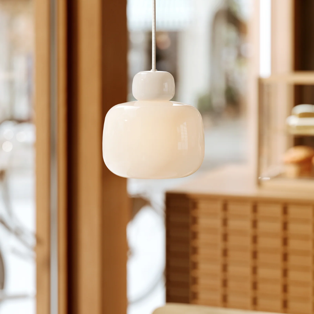 The Stone Glass Pendant in the size Small by Woud turned on in a cafe.
