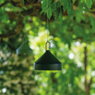 The black Amelie Pro Hanging Lamp from Zafferano in a garden.