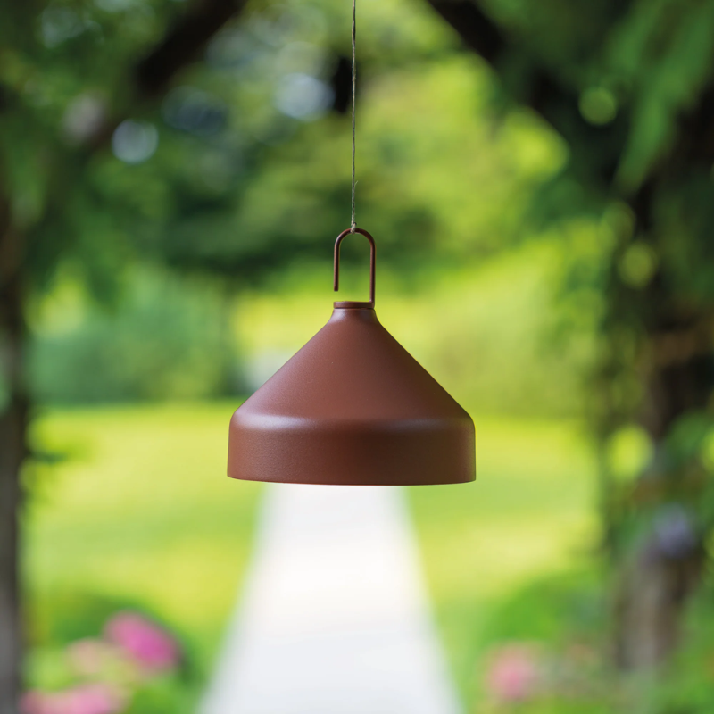 The terracotta Amelie Pro Hanging Lamp from Zafferano beside an outdoor pathway.
