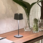 The dark gray Ofelia Pro cordless lamp from Zafferano in a lounge.