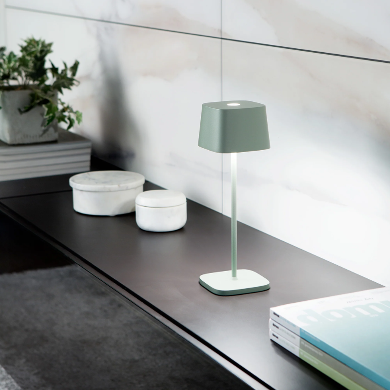 The sage Ofelia Pro cordless lamp from Zafferano in a living room.
