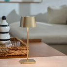 The satin brass Ofelia Pro cordless lamp from Zafferano on a coffee table.