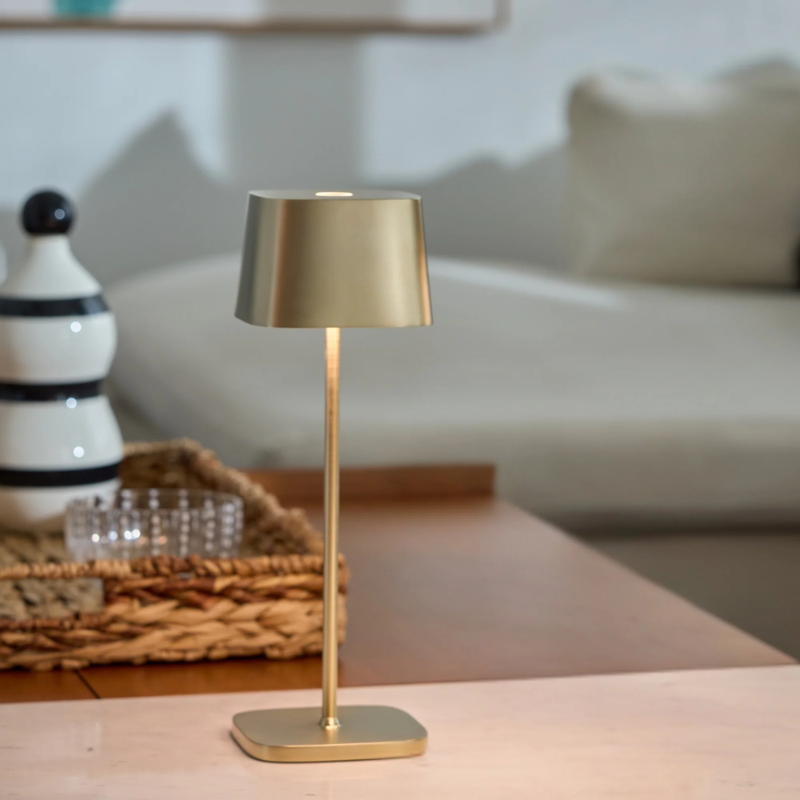 The satin brass Ofelia Pro cordless lamp from Zafferano on a coffee table.