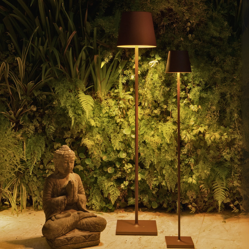 The rust Poldina Pro XXL Floor Lamp from Zafferano in a garden.
