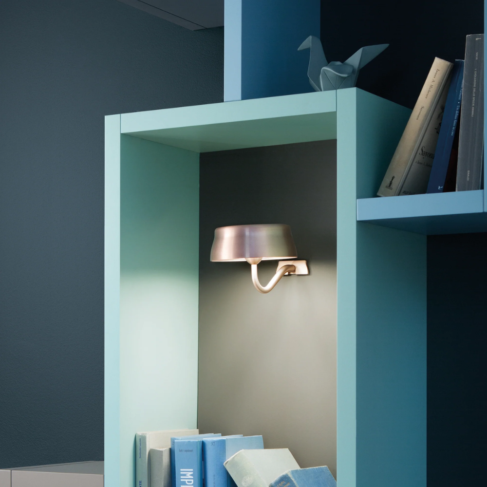 The anodized copper Sister Light Wi-Fi Wall Lamp from Zafferano within a shelf.