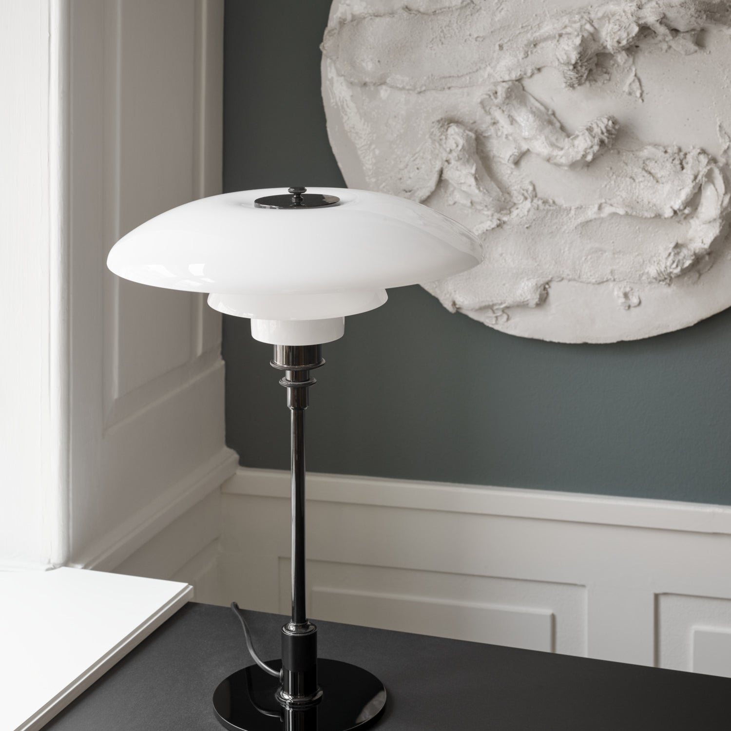 The PH 3½-2½ glass table lamp is designed based on the principle of a reflective three-shade system, which directs the majority of the light downwards. The shades are made of hand blown opal three-layer glass, which is glossy on top and sandblasted matte on the underside, giving a soft and diffused light distribution. Designed by Poul Henningsen.