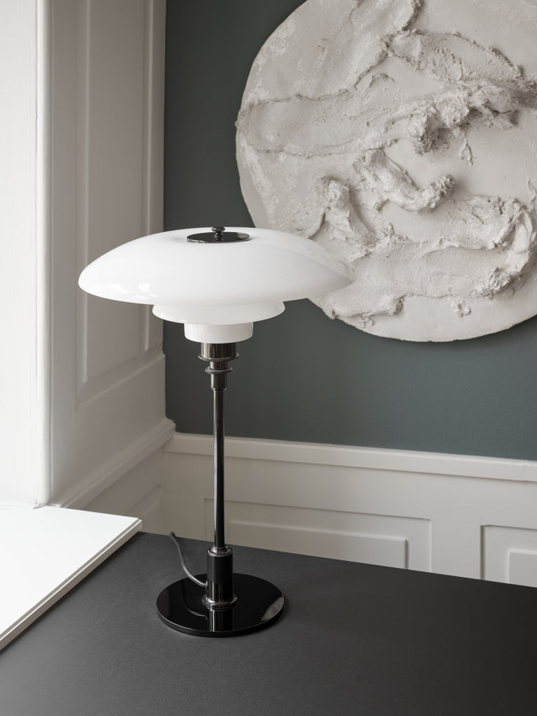 The PH 3½-2½ glass table lamp is designed based on the principle of a reflective three-shade system, which directs the majority of the light downwards. The shades are made of hand blown opal three-layer glass, which is glossy on top and sandblasted matte on the underside, giving a soft and diffused light distribution. Designed by Poul Henningsen.