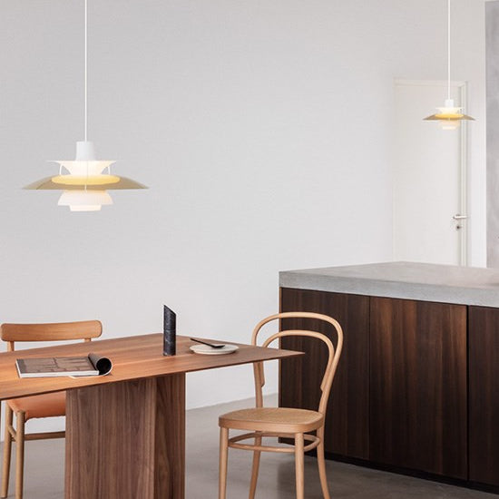 The PH 5 Pendant Light by Louis Poulsen in Brass over a wooden dining table