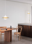 The PH 5 Pendant Light by Louis Poulsen in Brass over a wooden dining table