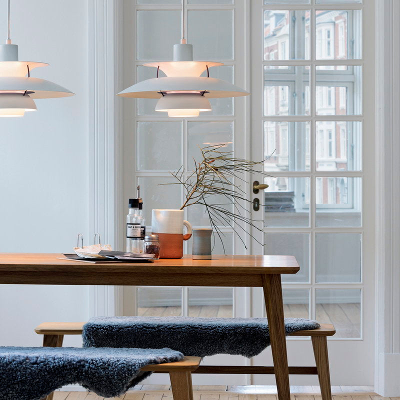 The PH 5 Pendant Light hangs above a wooden dining table 