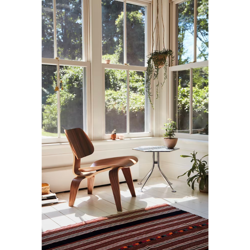 The Eames Molded Plywood Lounge Chair Wood Base (LCW) from Herman Miller in a lifestyle photograph in a lounge.