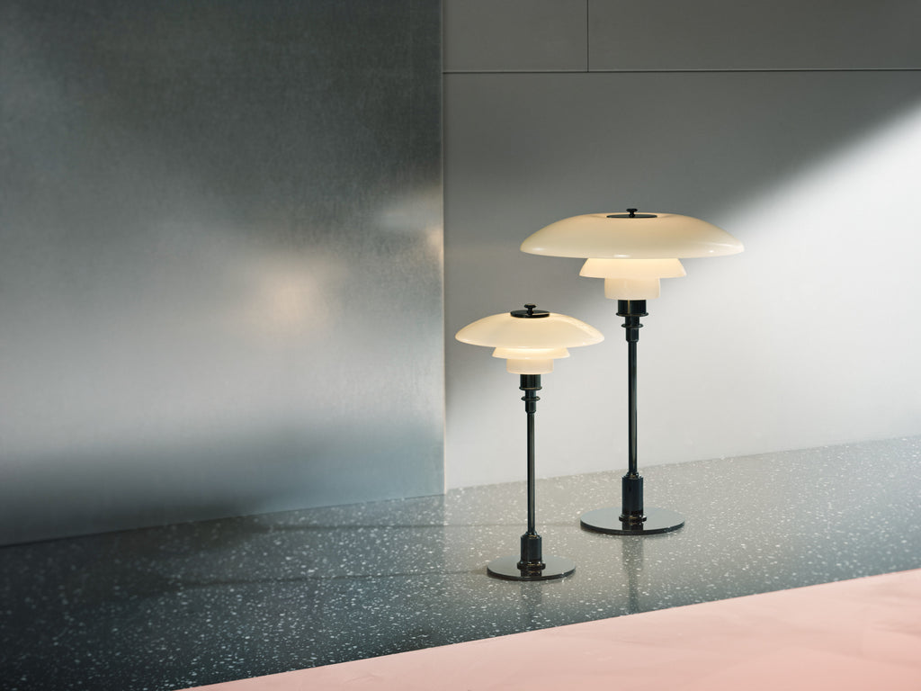 The PH 3½-2½ glass table lamp is designed based on the principle of a reflective three-shade system, which directs the majority of the light downwards. The shades are made of hand blown opal three-layer glass, which is glossy on top and sandblasted matte on the underside, giving a soft and diffused light distribution. Designed by Poul Henningsen.