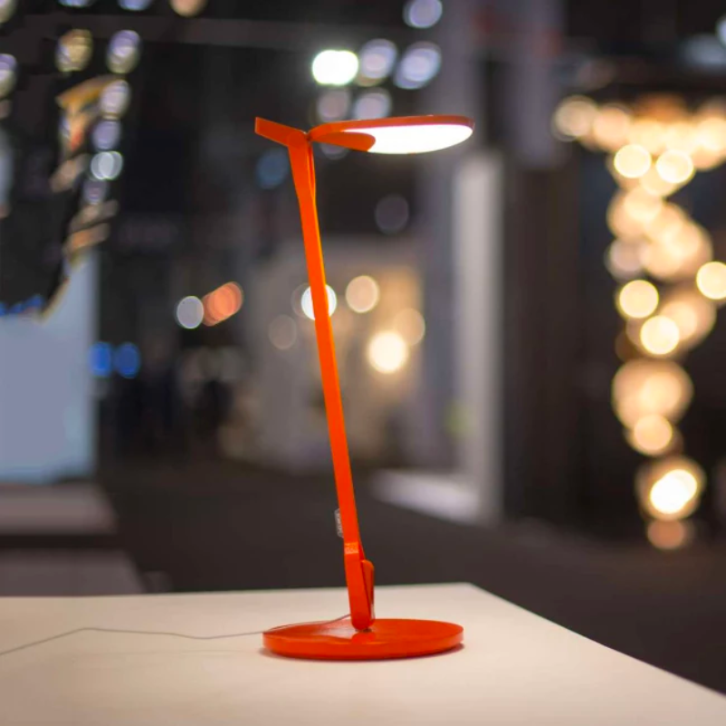The Splitty Desk Lamp from Koncept in matte orange in a living area.