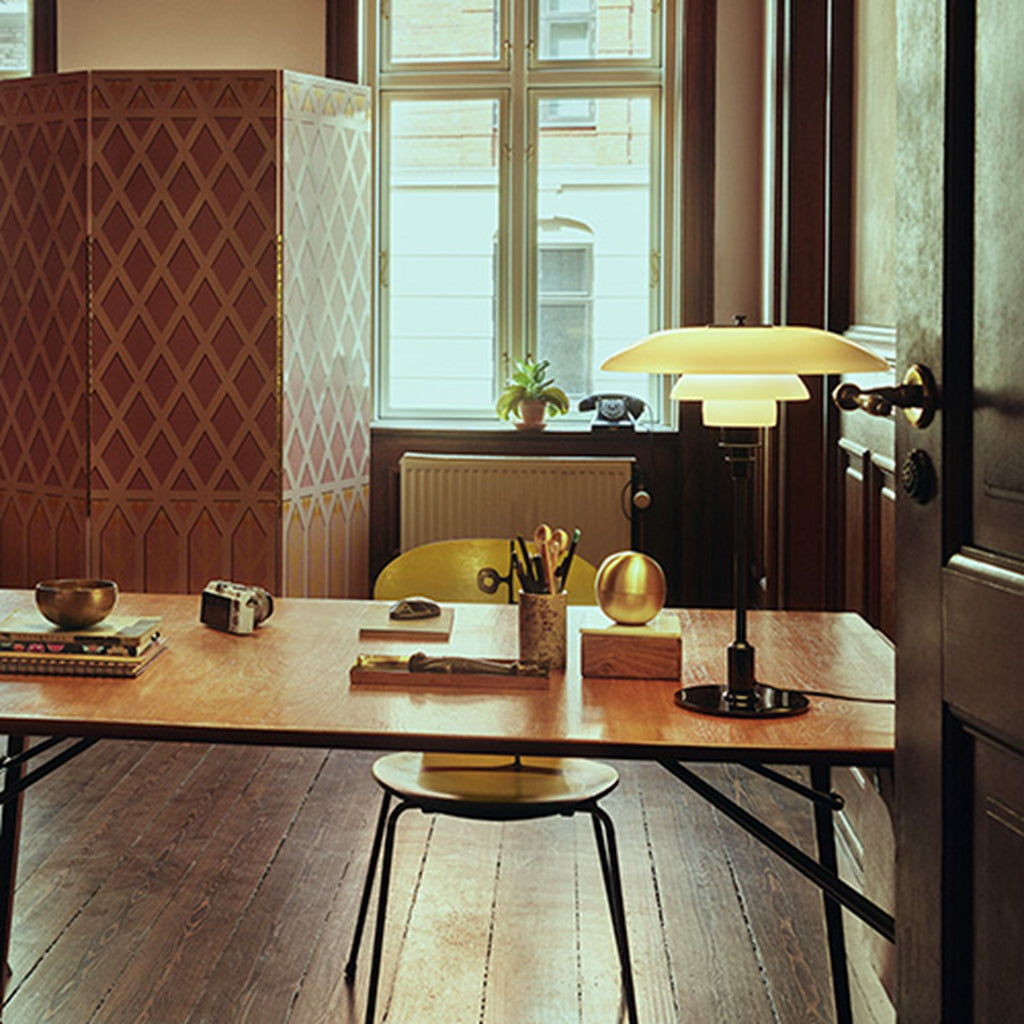 The PH 3½-2½ glass table lamp is designed based on the principle of a reflective three-shade system, which directs the majority of the light downwards. The shades are made of hand blown opal three-layer glass, which is glossy on top and sandblasted matte on the underside, giving a soft and diffused light distribution. Designed by Poul Henningsen.